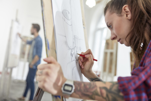 artista femenina enfocada con tatuajes dibujando